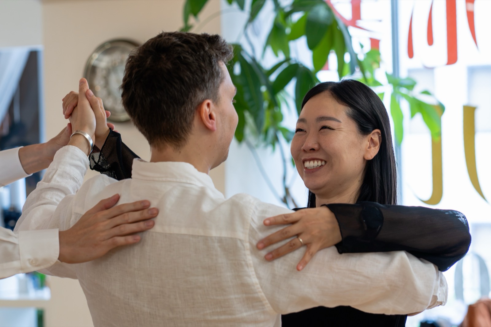 A couple laughing in hold during a ballroom lesson, while Koji gently guides them